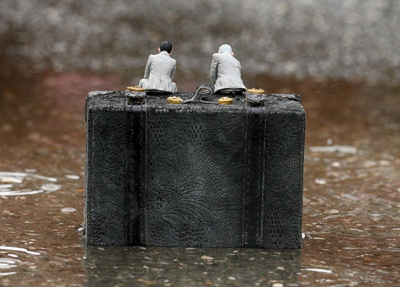 Two miniature figures sitting on a briefcase in the rain