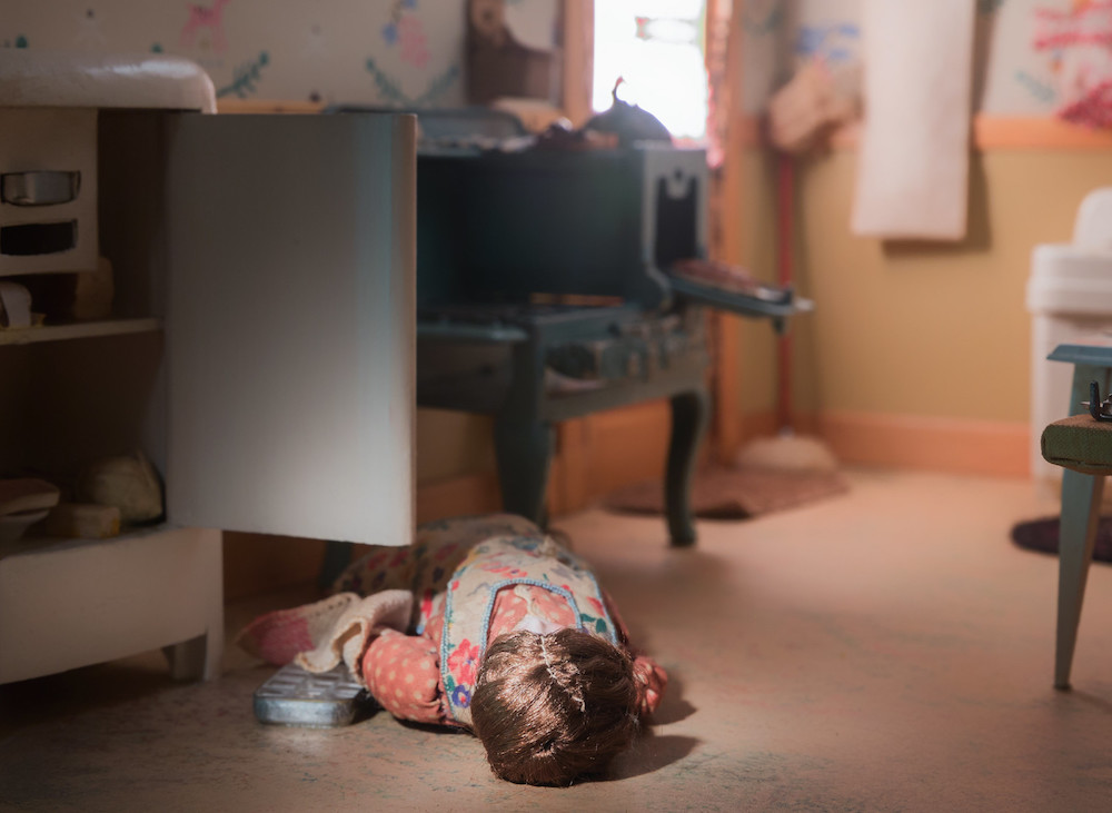 Diorama showing a woman lying on the floor of a kitchen