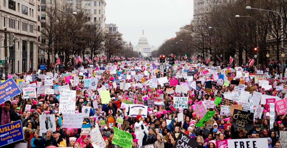 A crowd of women march and protest with the White House in the background