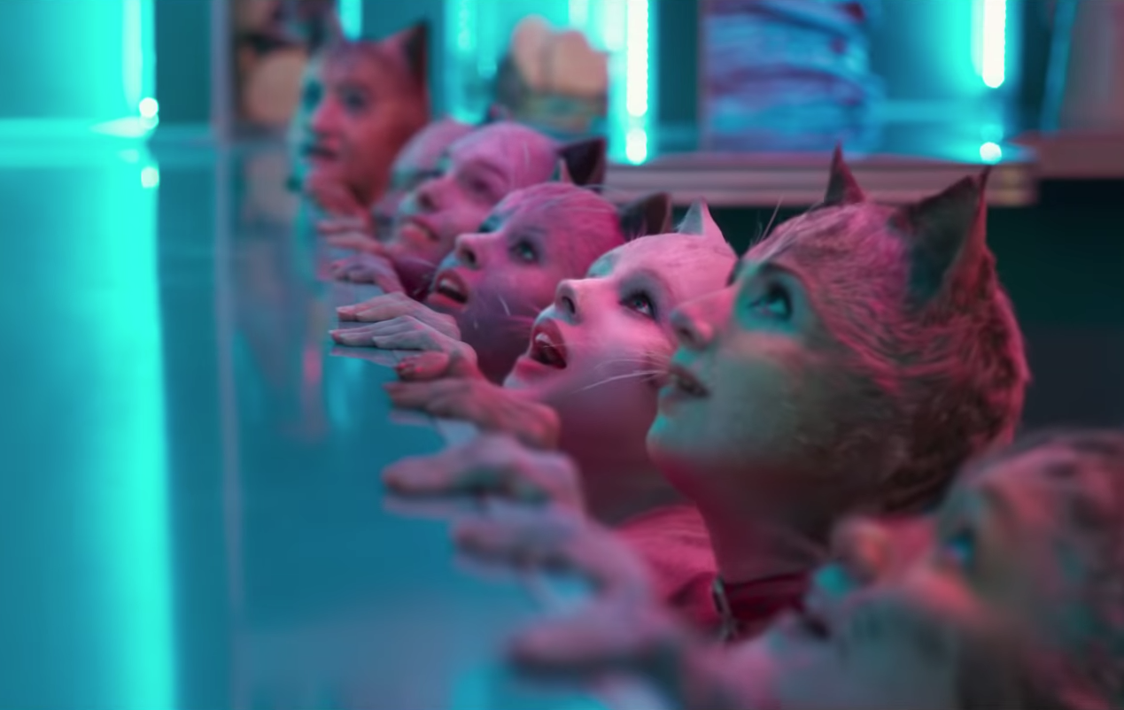 Several humanoid cats hold the edge of a counter and look up eagerly. It is horrible.