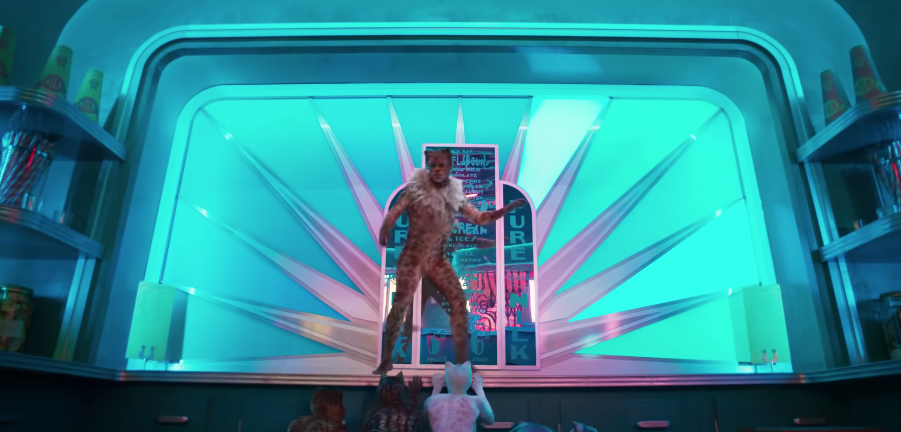 A person in a leopard-print cat costume dances on a human-size counter. It is horrible.