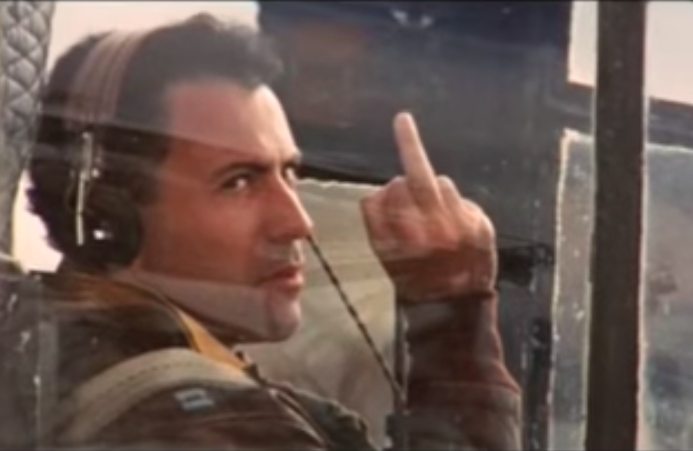 Yossarian sitting in an airplane ready to take off, giving the finger to the camera