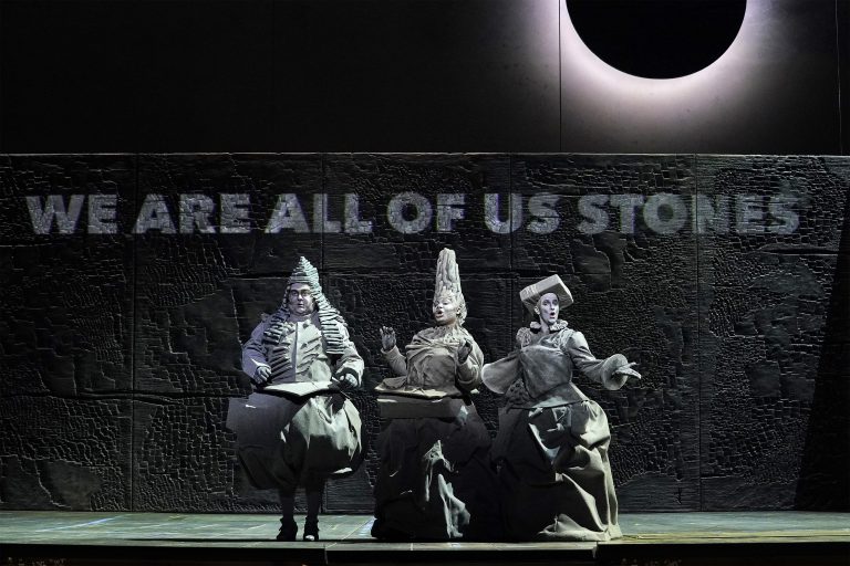 Three opera singers dressed in ornate grey outfits, playing stones in Matthew Aucoin's opera "Eurydice"