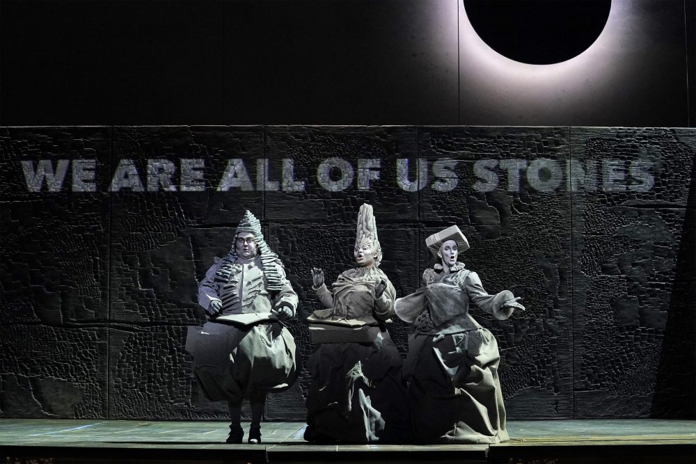 Three opera singers dressed in ornate grey outfits, playing stones in Matthew Aucoin's opera "Eurydice"