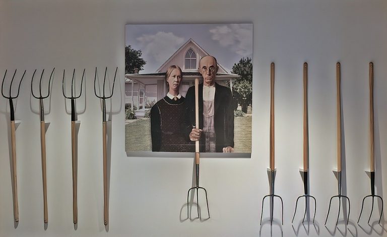 A poster of American Gothic surrounded by real pitchforks