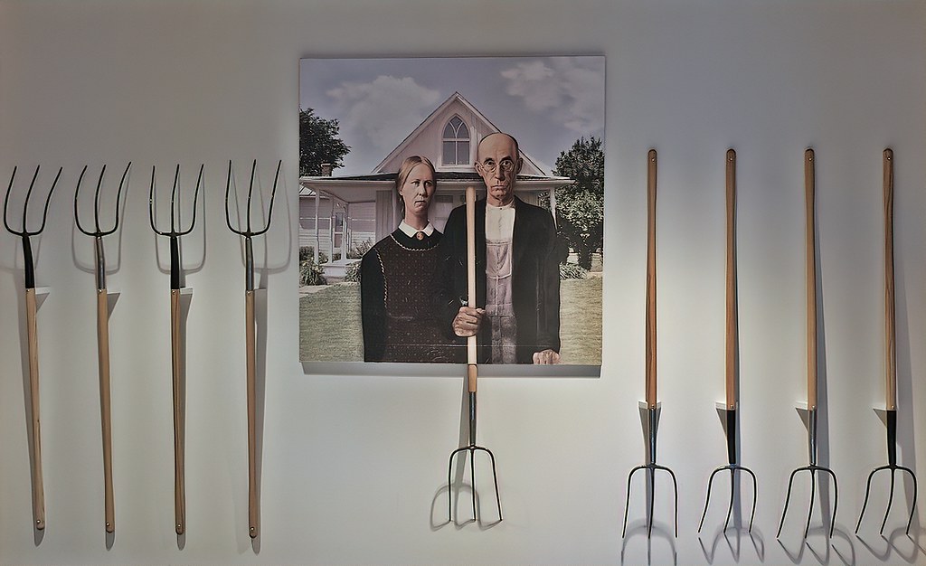 A poster of American Gothic surrounded by real pitchforks