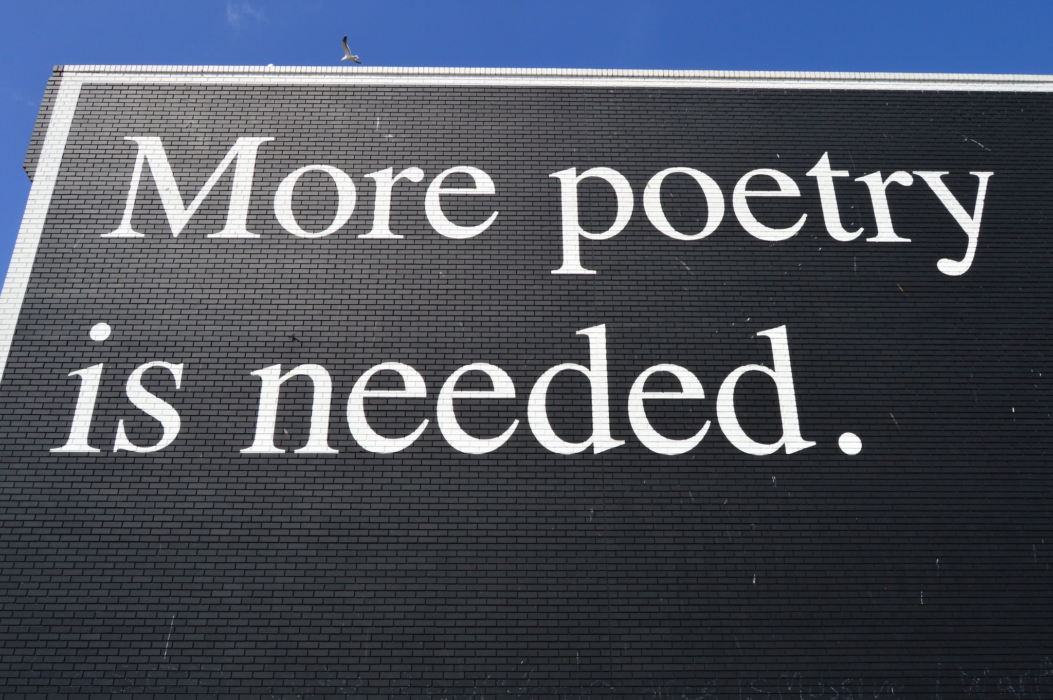 White text on black wall reading "more poetry is needed"
