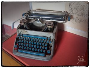Grey typewriter with blue keys on red desk