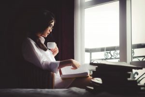 Asian woman reading with a cup of coffee by a window