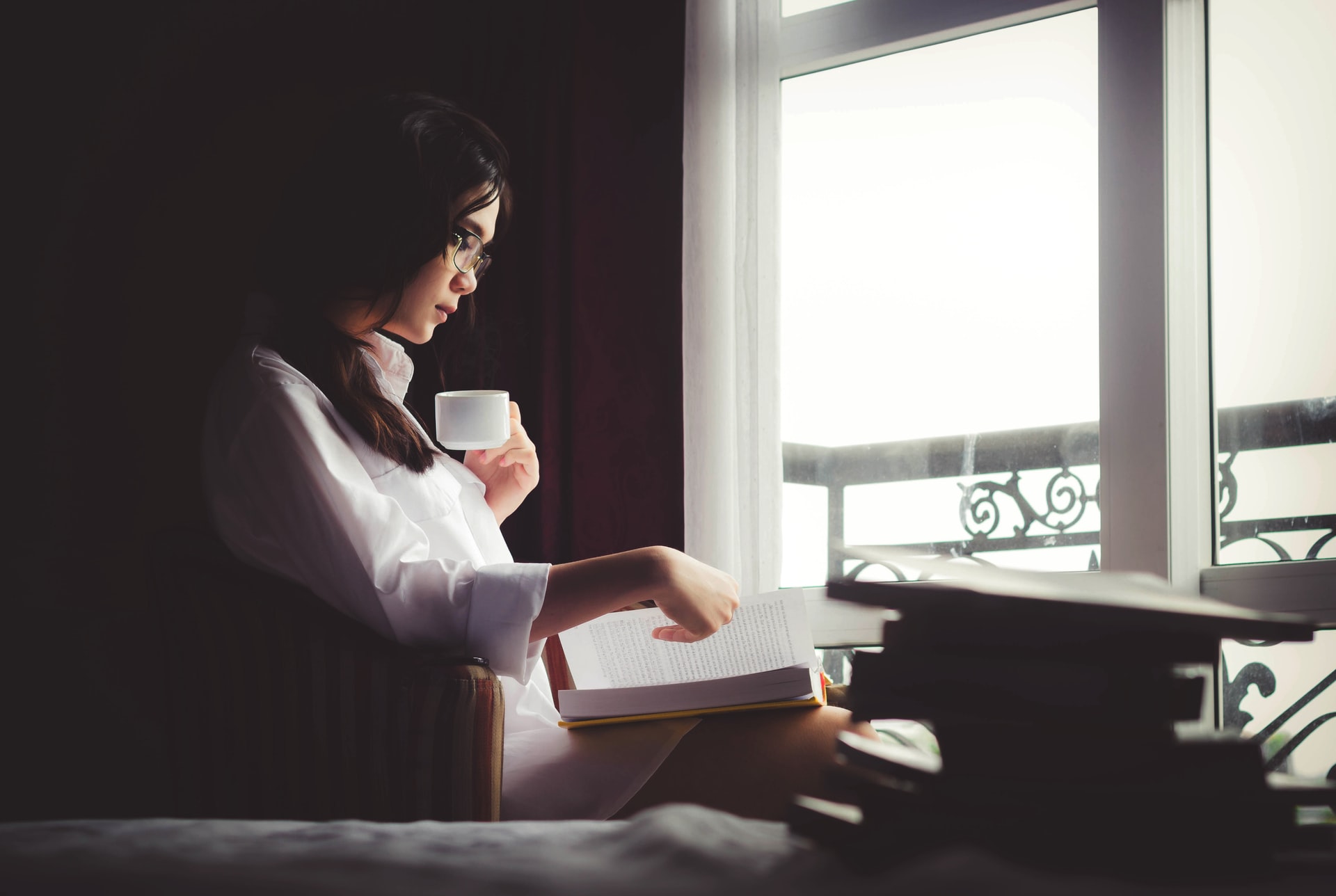 Asian woman reading with a cup of coffee by a window