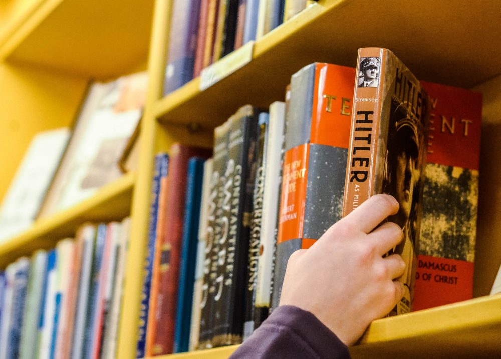 Hand putting a book with the word "Hitler" on the spine onto a bookshelf