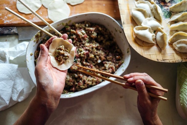 Older woman's hands filling a dumpling using chopsticks