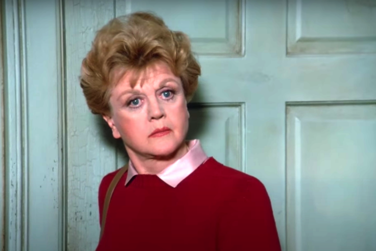 Screenshot from "Murder, She Wrote," showing Jessica Fletcher standing in front of a mint green door looking quizzical and wearing a pink collared blouse and maroon sweater