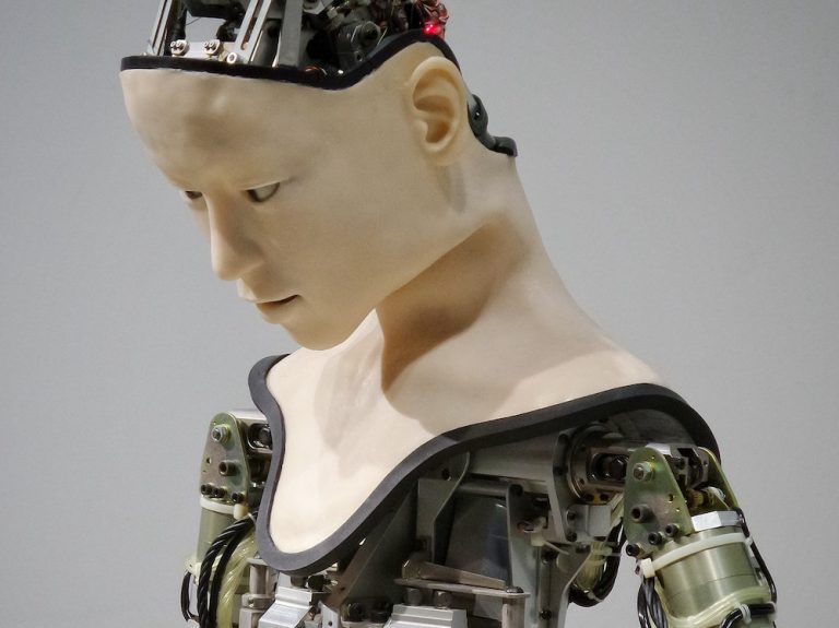 Android with a human-like skin on its face and neck but bare circuit boards on head, shoulders, and chest