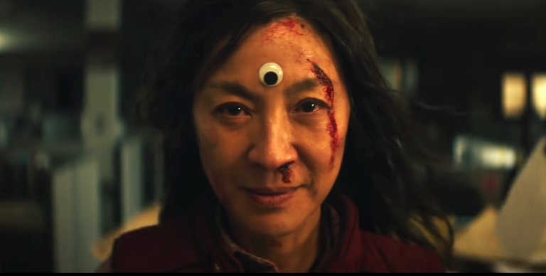 An Asian woman with blood on her face and a googly eye on her forehead stares at the camera