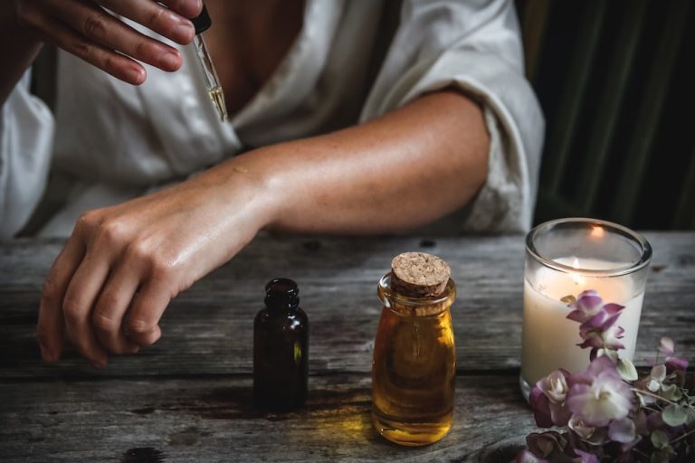 Woman dropping oil on her arm next to candle and flowers