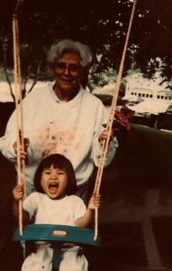 The author as a child playing in a swing with their grandmother behind them.