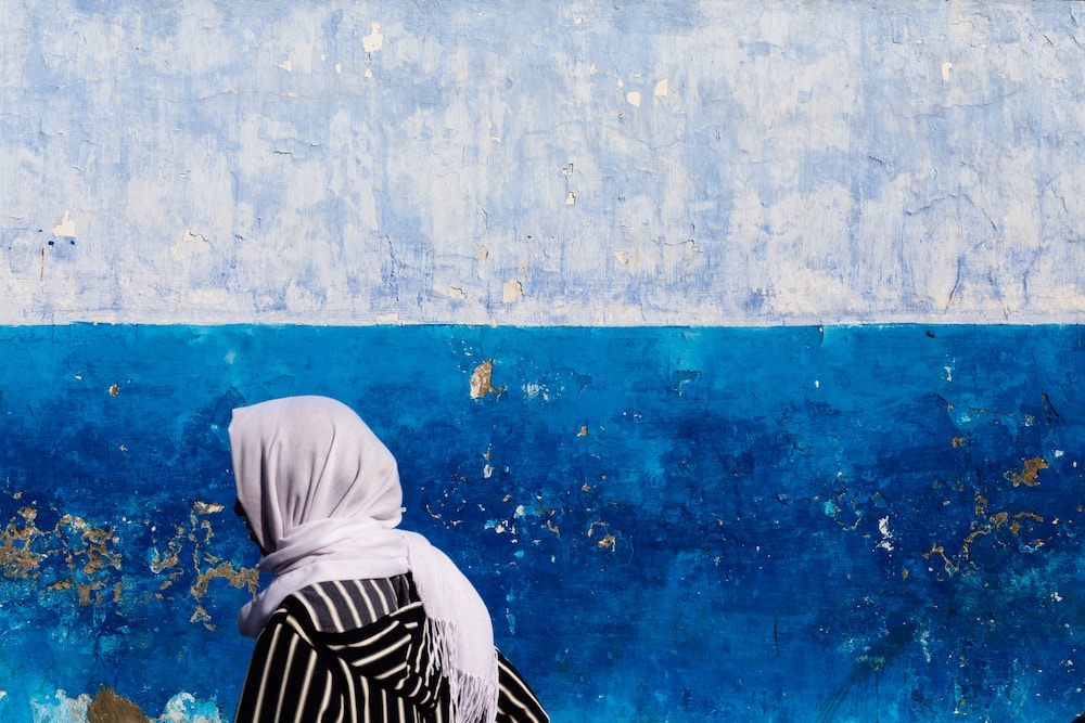 person wearing hijab walking in front of an aquamarine painted wall