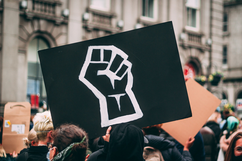 A person at a protest holds a sign with a fist drawn on it