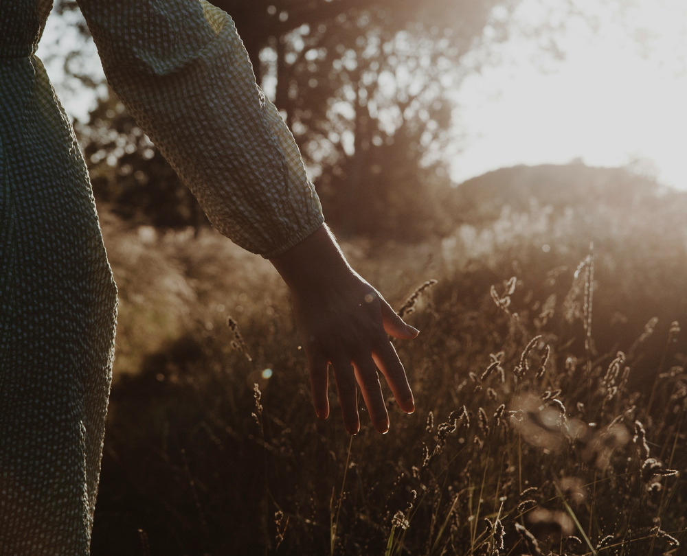A woman in a gray long sleeve shirt stands in a green grass field