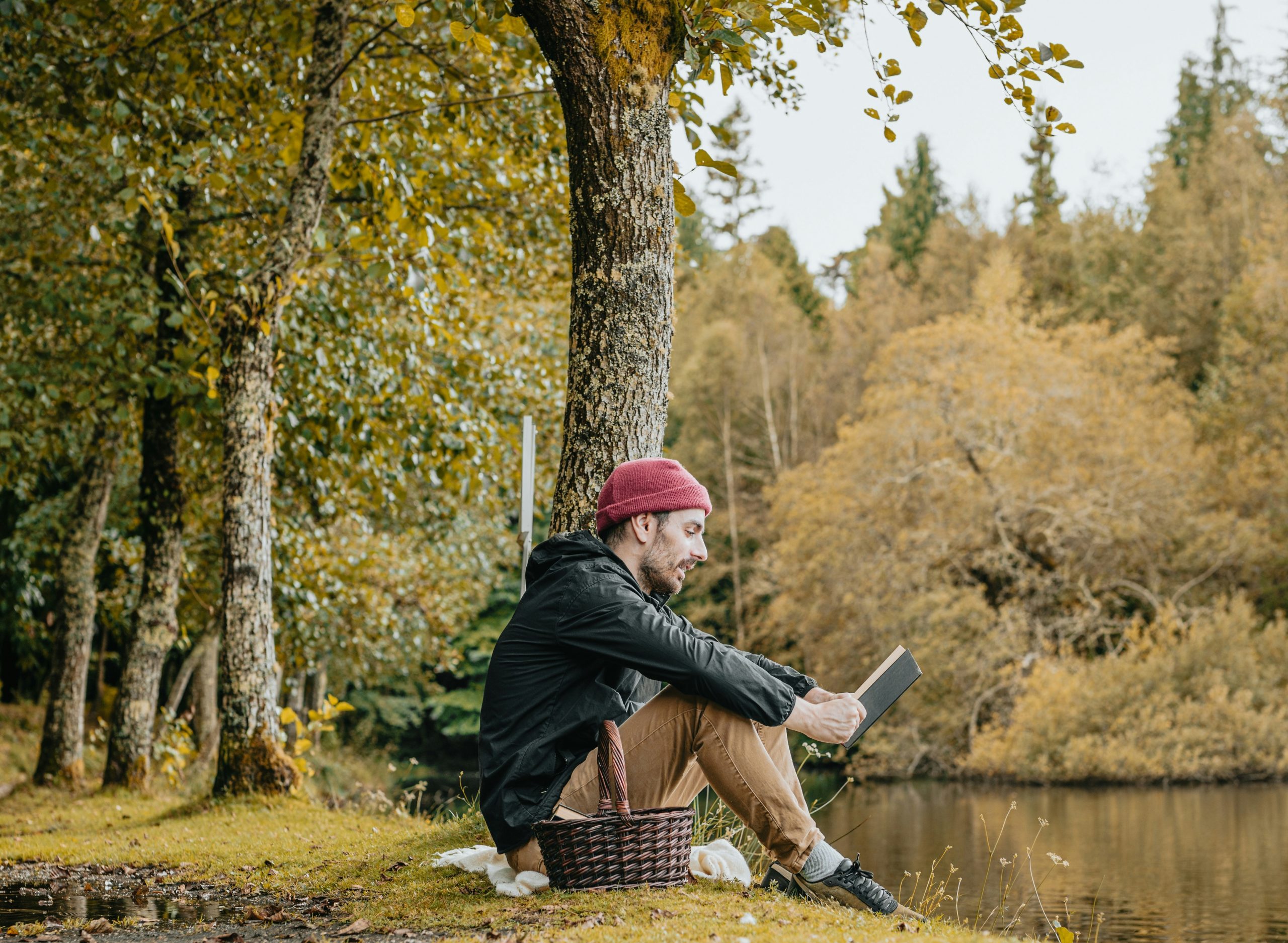 A man sitting by a strean reading in fall.