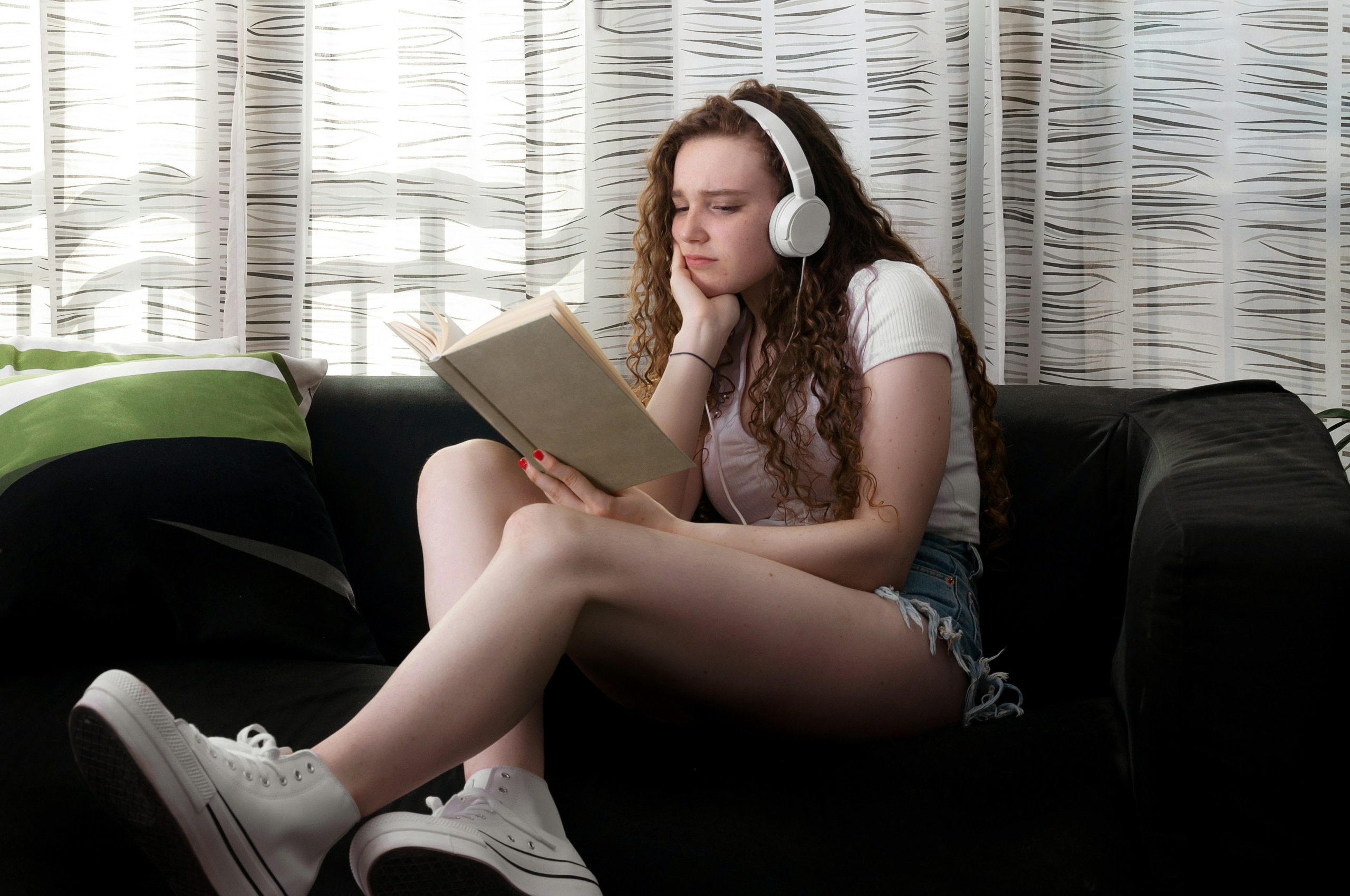 Photo of young woman reading a book and wearing headphones