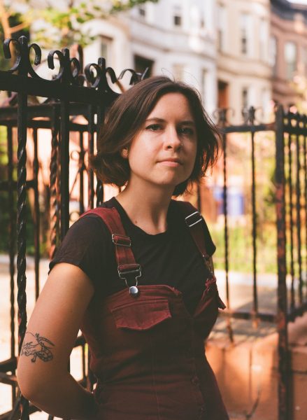A person in overalls with short hair looking into the camera