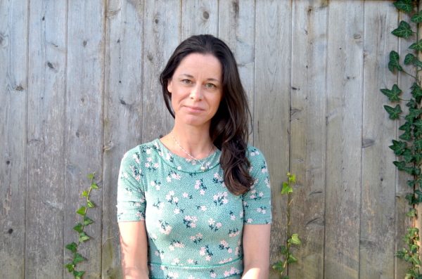 author against a wood backdrop in a green shirt looking into the camera