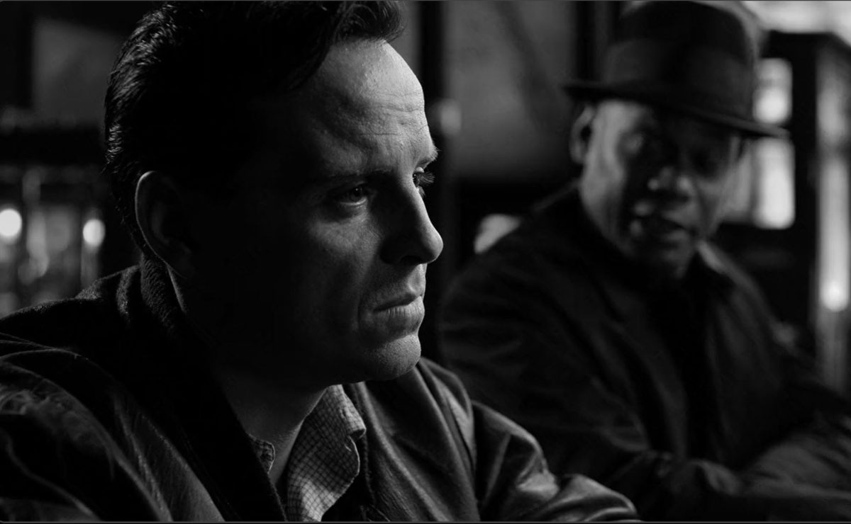 Profile of a man in the forefront at a bar and another at the back looking at the first man -- black and white image
