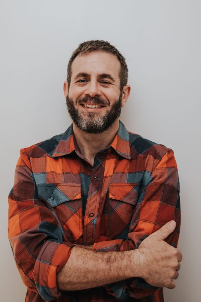 Author, Case Q. Kerns, in a plaid shirt and cropped hair smiling into the camera